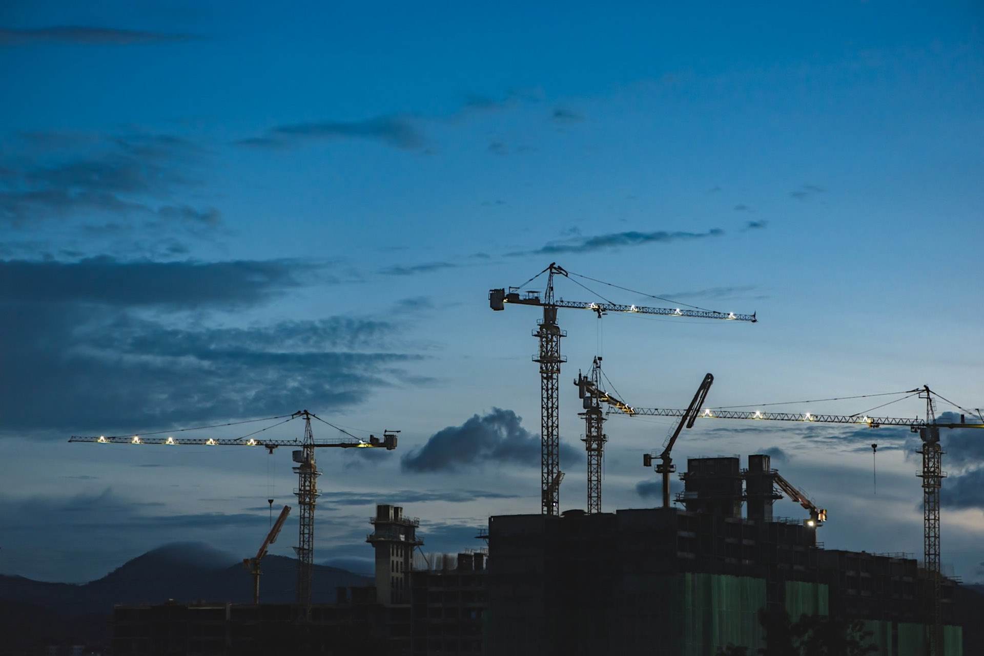Tower cranes silhouetted over a city construction site at dusk